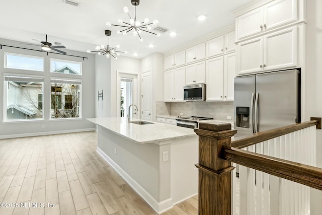 kitchen with an island with sink, white cabinets, stainless steel appliances, and a sink