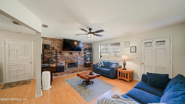 living area with ceiling fan, a fireplace, wood finished floors, and visible vents