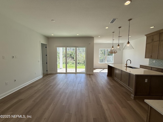 kitchen featuring pendant lighting, sink, dark wood-type flooring, an island with sink, and decorative backsplash