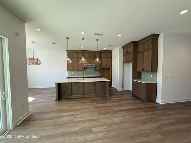 kitchen with sink, decorative light fixtures, light hardwood / wood-style floors, and a center island with sink