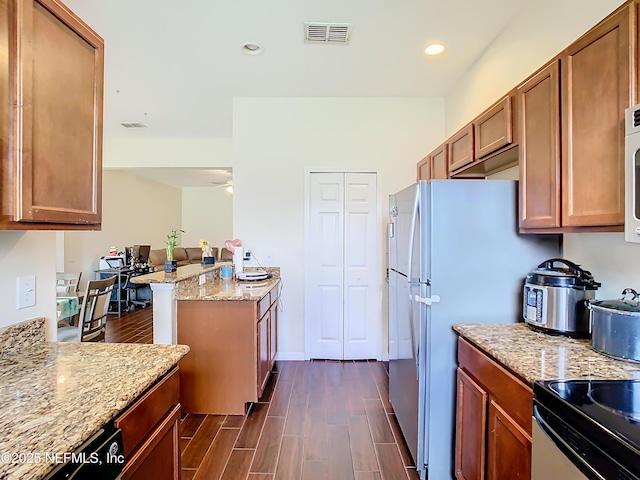 kitchen featuring visible vents, light stone counters, brown cabinets, a peninsula, and wood finish floors