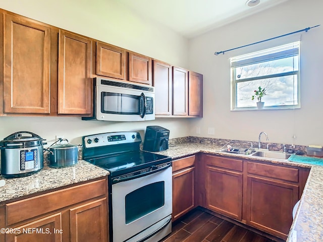 kitchen with dark wood-style floors, brown cabinets, light stone countertops, stainless steel appliances, and a sink