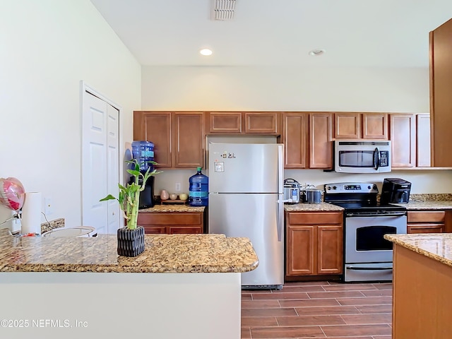 kitchen featuring visible vents, brown cabinets, light stone countertops, stainless steel appliances, and wood finish floors