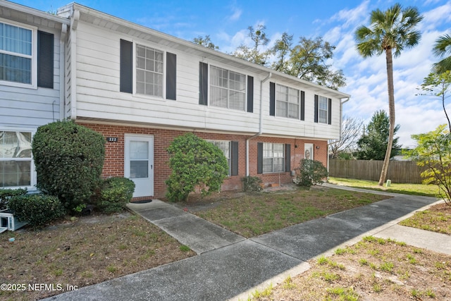 view of property with brick siding, a front lawn, and fence