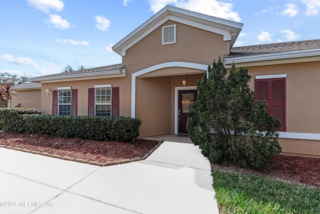 doorway to property featuring a shingled roof and stucco siding