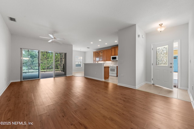 unfurnished living room featuring baseboards, visible vents, ceiling fan, and light wood finished floors