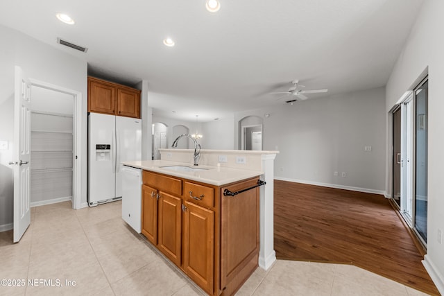 kitchen with light tile patterned floors, a kitchen island with sink, white appliances, open floor plan, and light countertops