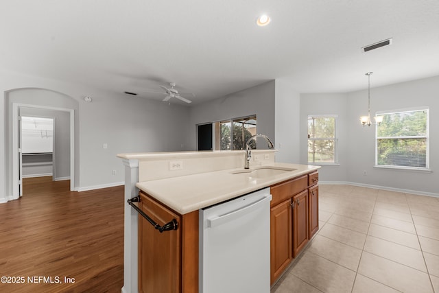 kitchen with white dishwasher, a kitchen island with sink, a sink, visible vents, and light countertops