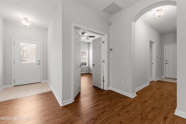 entryway with arched walkways, visible vents, baseboards, and wood finished floors