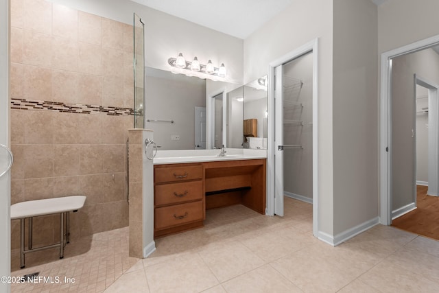 bathroom featuring baseboards, tile patterned flooring, a spacious closet, vanity, and a walk in shower