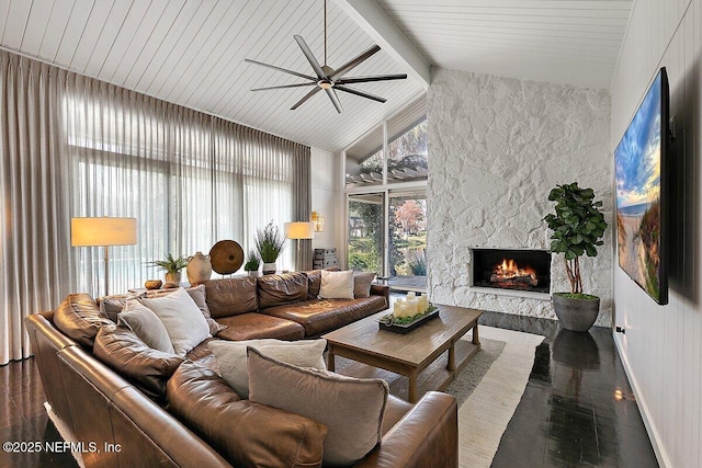 living area with ceiling fan, high vaulted ceiling, a stone fireplace, wood finished floors, and beamed ceiling