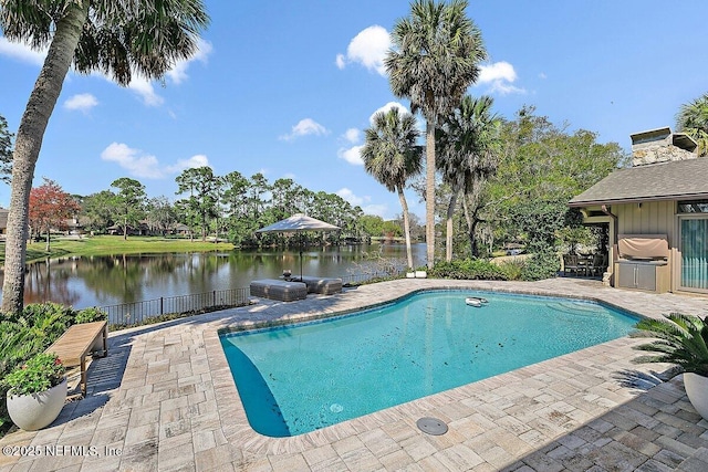 outdoor pool featuring grilling area, a patio area, fence, and a water view