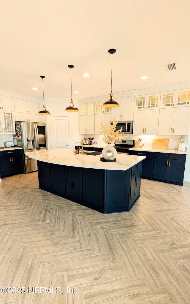 kitchen featuring a large island with sink, decorative light fixtures, stainless steel appliances, and white cabinets