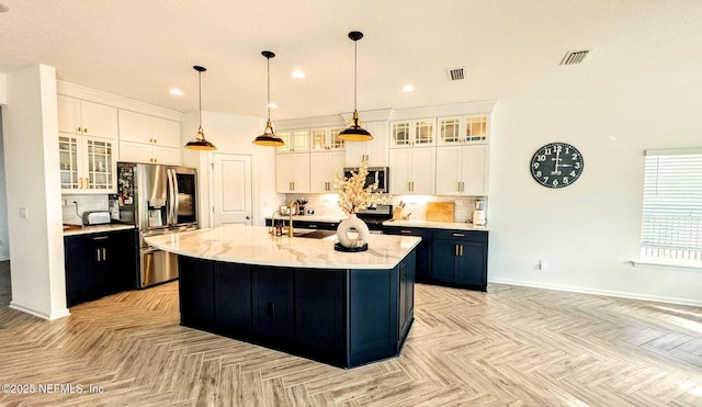 kitchen with light parquet flooring, appliances with stainless steel finishes, a kitchen island with sink, and white cabinets