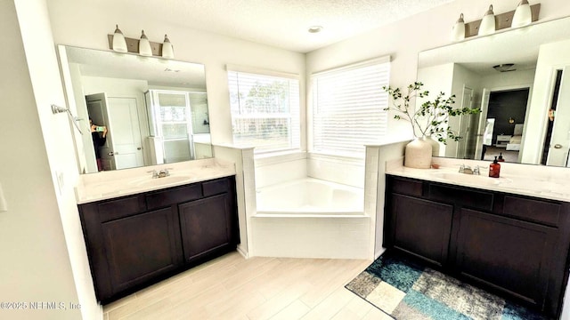 bathroom with tiled tub, vanity, wood-type flooring, and a textured ceiling