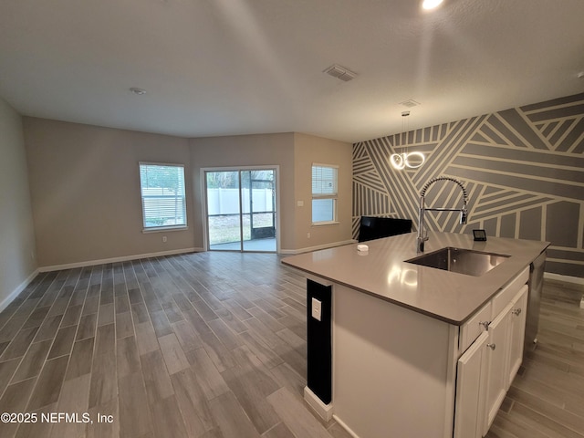 kitchen featuring a sink, visible vents, white cabinets, open floor plan, and a center island with sink