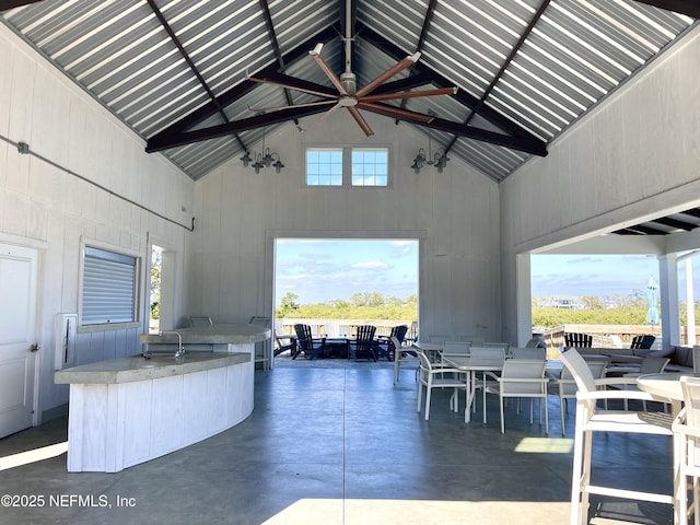 kitchen featuring ceiling fan, high vaulted ceiling, an island with sink, and concrete flooring