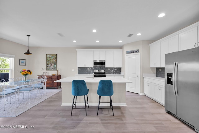 kitchen with appliances with stainless steel finishes, a kitchen island with sink, white cabinetry, recessed lighting, and backsplash