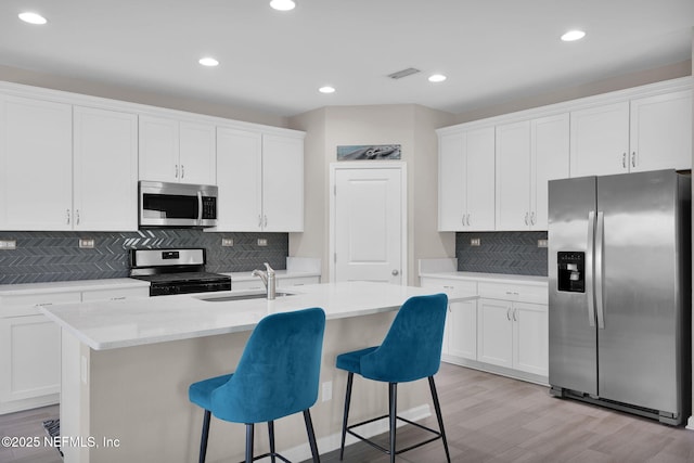 kitchen featuring an island with sink, white cabinetry, decorative backsplash, stainless steel appliances, and a sink