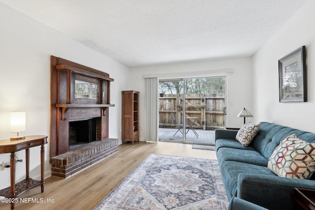 living room with light wood-type flooring, a brick fireplace, and a textured ceiling