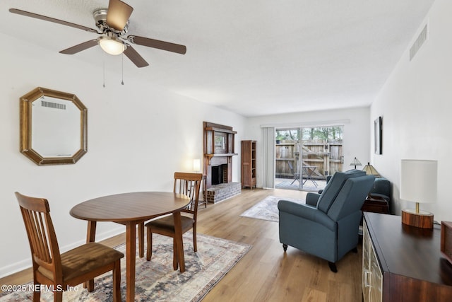 dining area with a fireplace, ceiling fan, and light wood-type flooring