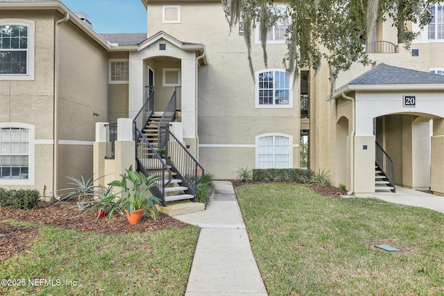 view of front facade featuring stairs, a front lawn, and stucco siding