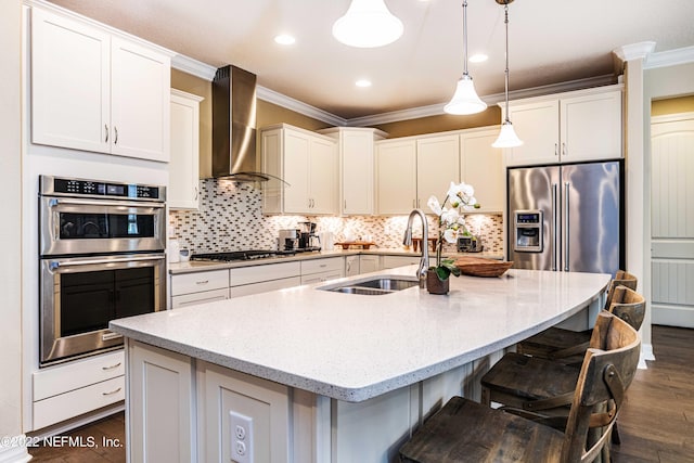 kitchen featuring sink, an island with sink, stainless steel appliances, and wall chimney range hood