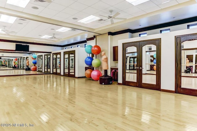 exercise room with a drop ceiling, ceiling fan, french doors, and hardwood / wood-style floors