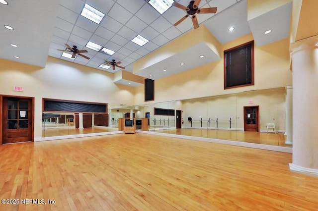 exercise room with light wood-type flooring, ornate columns, a towering ceiling, and ceiling fan