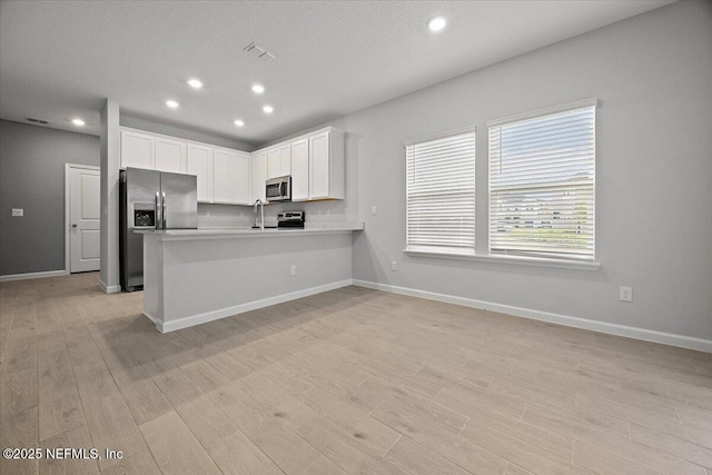 kitchen featuring baseboards, a peninsula, light wood-style flooring, white cabinets, and appliances with stainless steel finishes