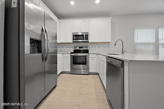 kitchen with light stone counters, appliances with stainless steel finishes, a peninsula, white cabinetry, and a sink