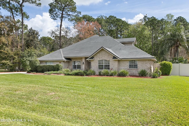 view of front of home featuring roof with shingles, fence, a front lawn, and brick siding