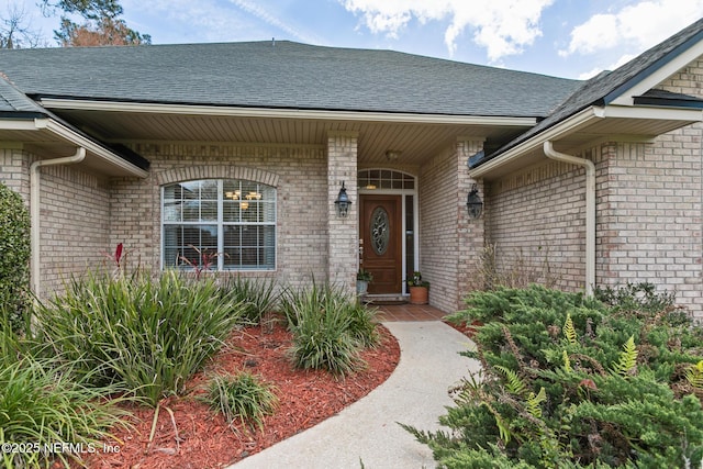 view of exterior entry with brick siding and roof with shingles