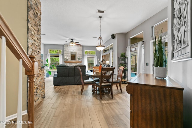 dining room featuring light wood finished floors, visible vents, a brick fireplace, ceiling fan, and a textured ceiling