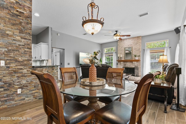 dining room with ceiling fan, a brick fireplace, visible vents, and wood tiled floor