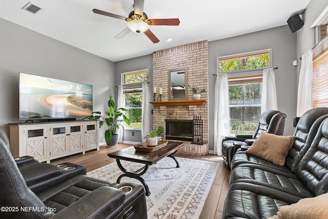 living room with a healthy amount of sunlight, a brick fireplace, visible vents, and wood finished floors