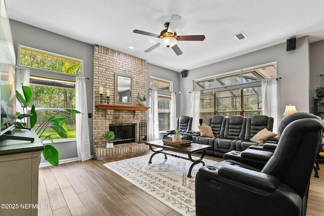 living area with a textured ceiling, ceiling fan, wood finished floors, visible vents, and a brick fireplace