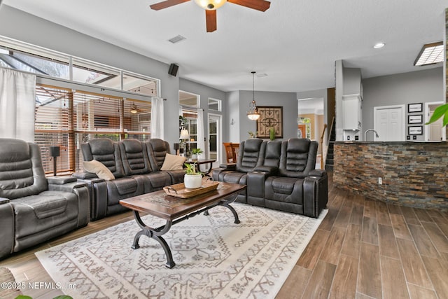 living area featuring a ceiling fan, visible vents, a textured ceiling, and wood finished floors