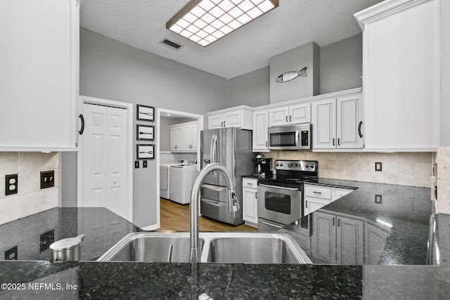 kitchen with visible vents, decorative backsplash, stainless steel appliances, separate washer and dryer, and a sink