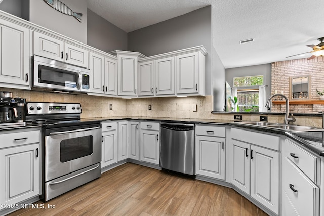 kitchen featuring appliances with stainless steel finishes, dark countertops, a sink, and light wood-style floors