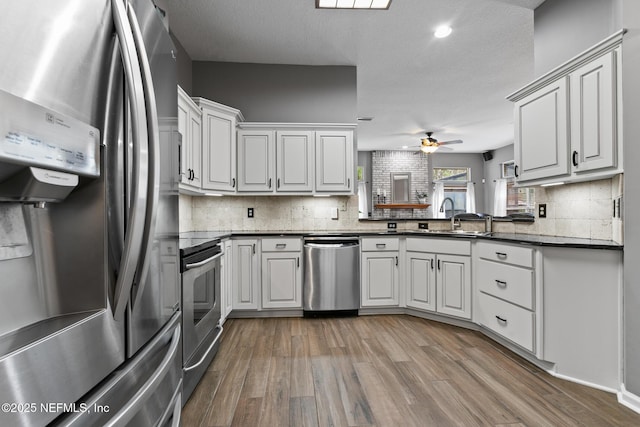 kitchen with stainless steel appliances, dark countertops, a sink, ceiling fan, and wood finished floors