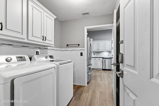 laundry room with cabinet space, visible vents, washing machine and clothes dryer, a textured ceiling, and light wood-type flooring