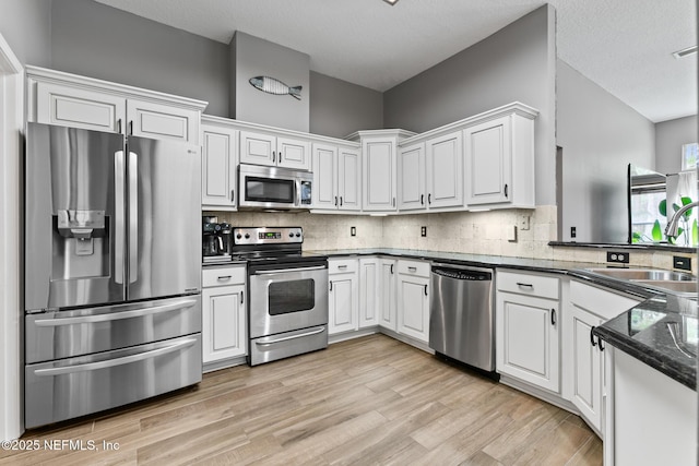 kitchen featuring stainless steel appliances, tasteful backsplash, light wood-style flooring, white cabinetry, and a sink