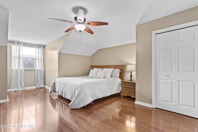 bedroom with a textured ceiling, baseboards, vaulted ceiling, and wood finished floors