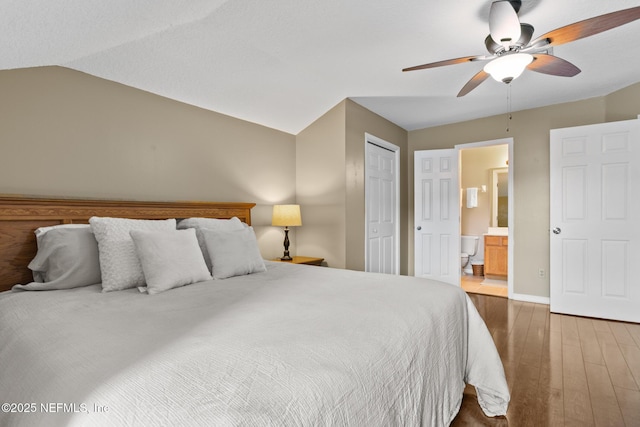 bedroom with lofted ceiling, ceiling fan, ensuite bath, wood finished floors, and baseboards