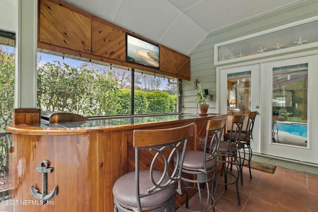 bar featuring tile patterned flooring, wooden walls, indoor bar, vaulted ceiling, and french doors