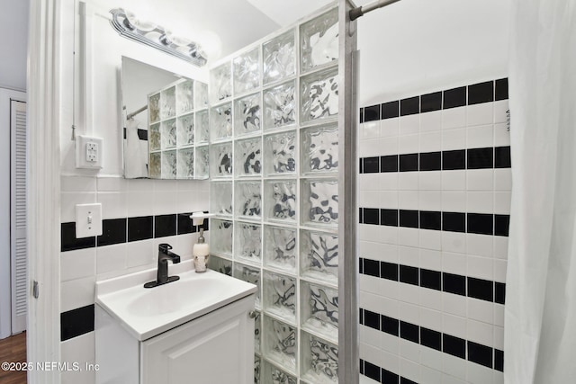 bathroom with tile walls, a tile shower, vanity, and tasteful backsplash