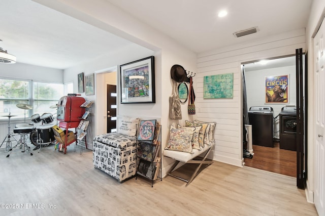 living area featuring light wood-type flooring, separate washer and dryer, and wooden walls