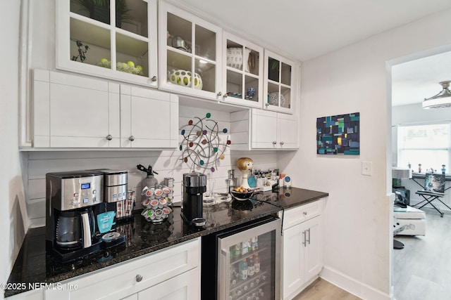 bar featuring white cabinetry, light hardwood / wood-style flooring, wine cooler, dark stone countertops, and decorative backsplash