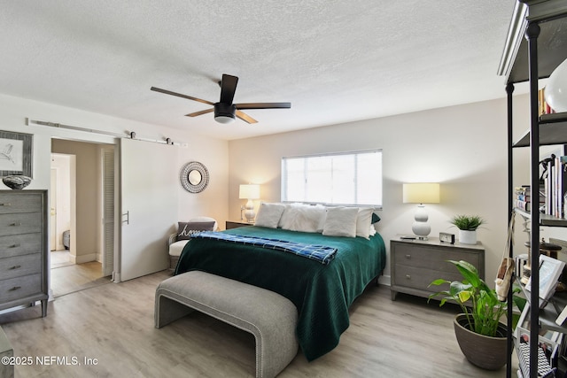 bedroom featuring light hardwood / wood-style floors, ceiling fan, a barn door, and a textured ceiling